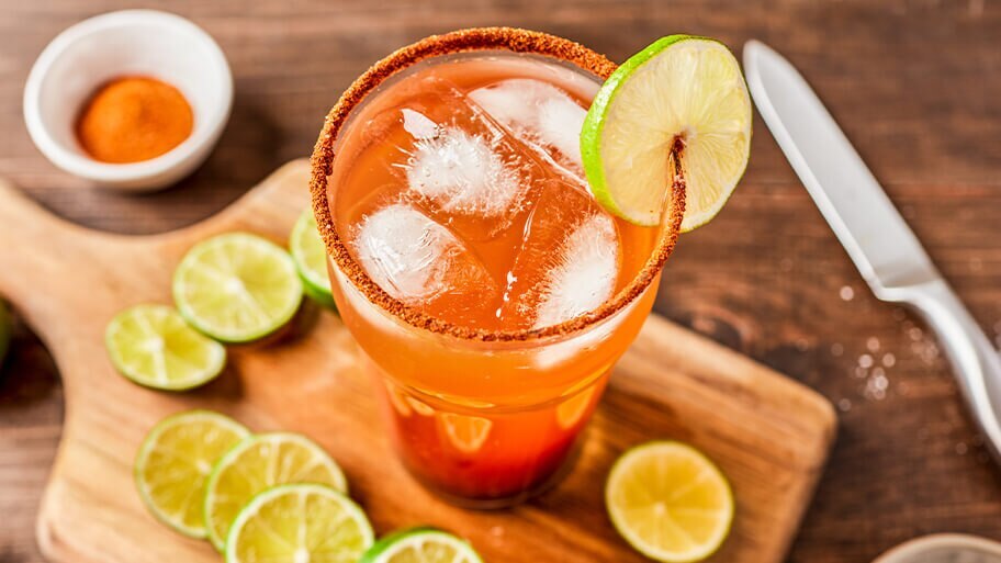 Overhead shot of a glass of bloody beer with chili powdered rim on a wood cutting board with fresh sliced lime.