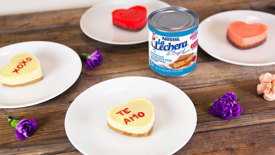 Mini cheesecakes with Te Amo and XOXO written in icing surrounding a can of La Lechera sweetened condensed milk.