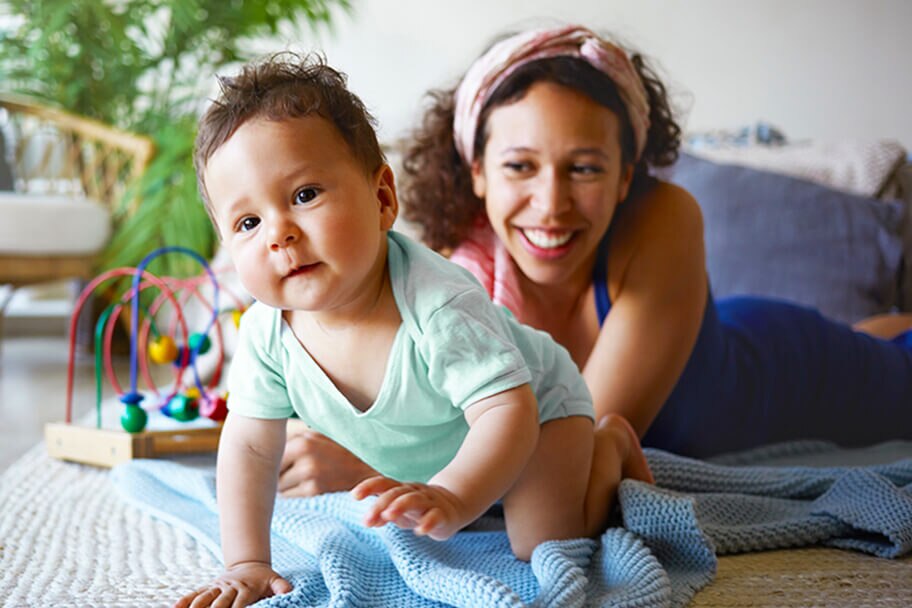 Woman smiling at a crawling child in a playroom.