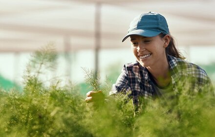 A female farmer smiling while inspecting her green crop.