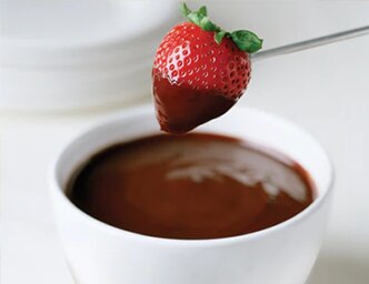 A skewer dips a strawberry into a bowl of chocolate fondue.