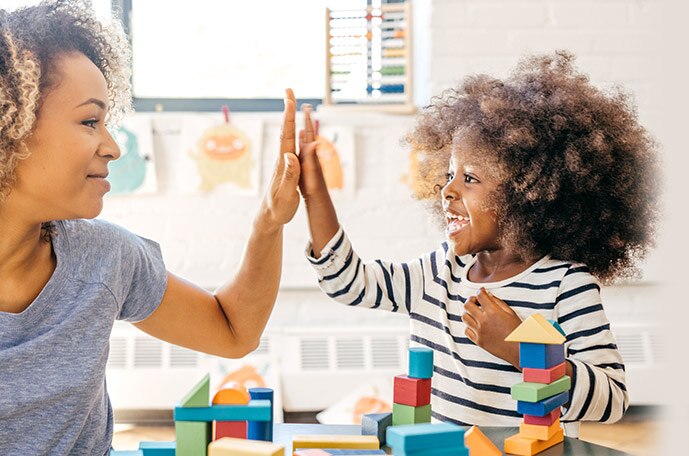 A mom and her daughter high five as they play with building blocks.