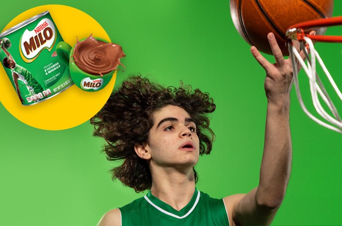 A teen boy in a green jersey tips a basketball into a hoop.