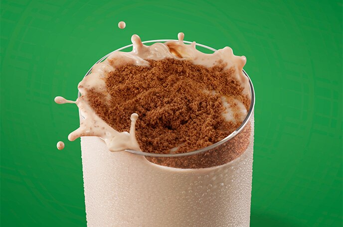 Polvo de MILO salpica y se arremolina en un vaso de leche sobre un fondo verde.