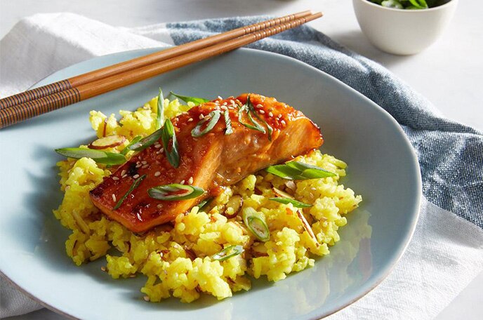 Glazed salmon over yellow seasoned rice on a blue plate with chopsticks.
