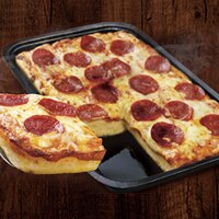 A pepperoni crispy pan pizza cut into square on a pan and wooden surface.