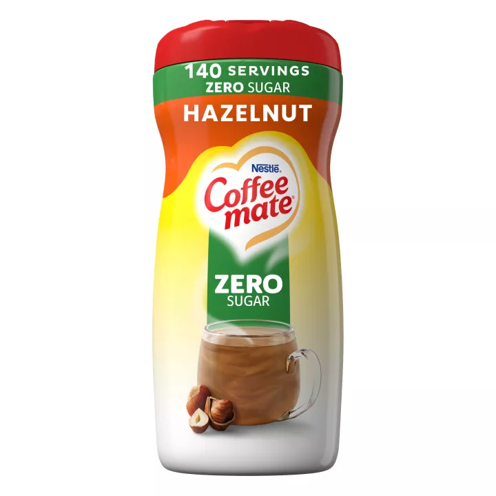 A canister of Hazelnut Powder with a green “sugar free” label above a coffee mug, whole hazelnuts and the product logo.