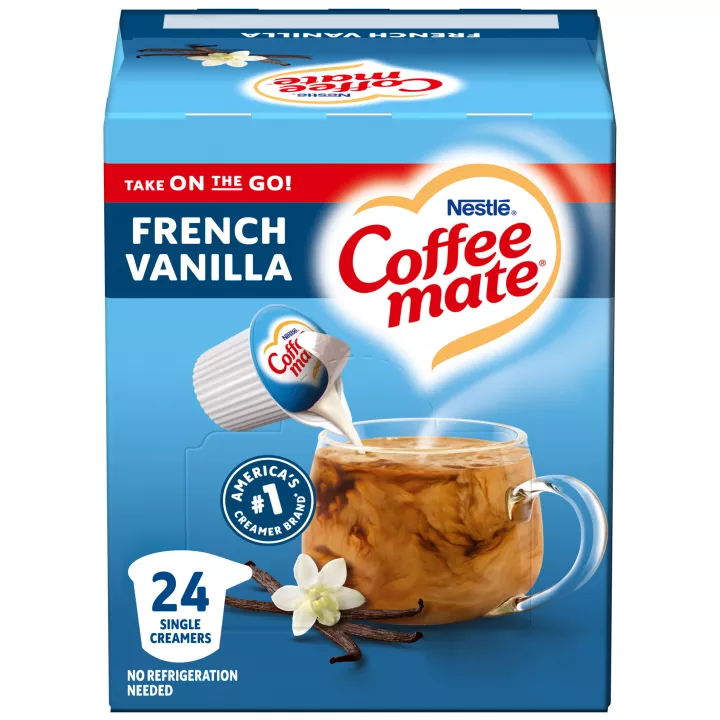 Una caja azul de porciones individuales de creamer Coffee mate Vanilla con una etiqueta azul encima de una taza de café, vaina de vainillas y el logotipo del producto.