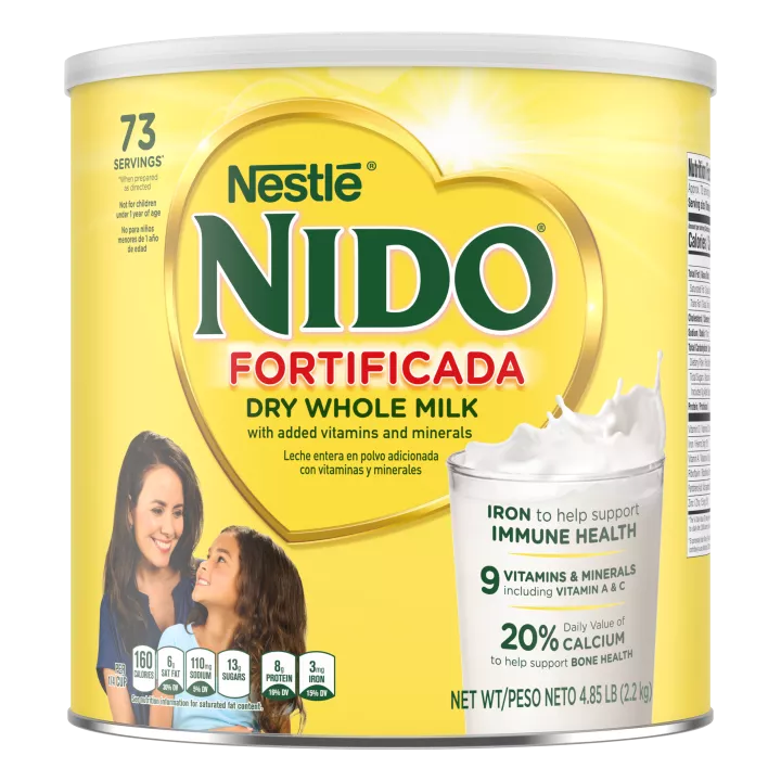 A canister of NIDO Fortificada with a yellow label, white lid and gold heart above a glass with milk being poured into it.