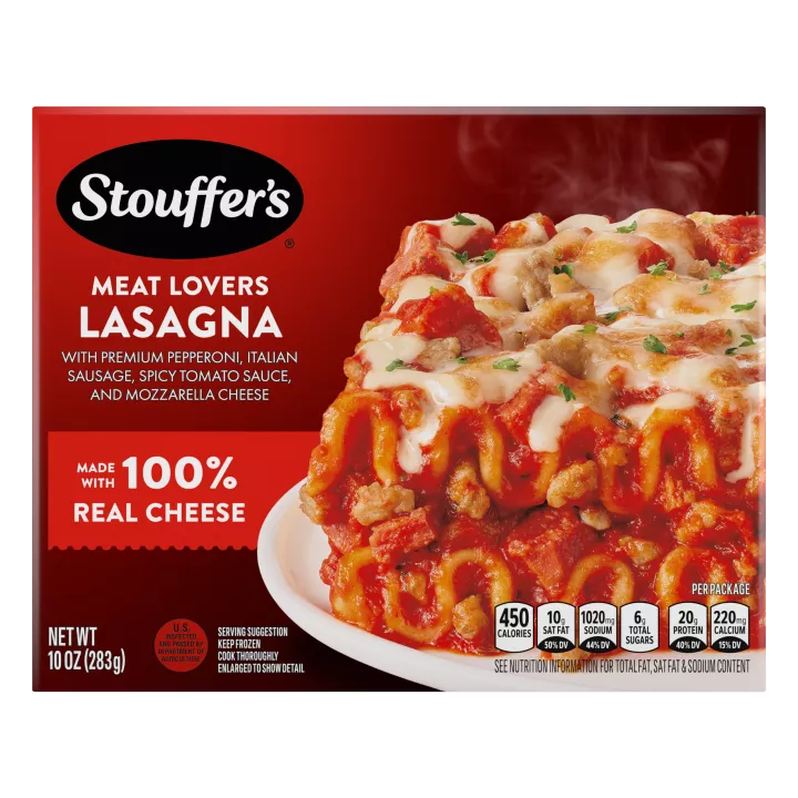 A plate of Meat Lovers Lasagna on a table below the product name, STOUFFER'S logo and "4 Delicious Meats" label.