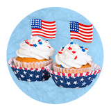 Close up of two cupcakes decorated for independence day with two mini flags sticking out of them , on a blue background.