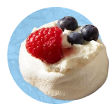 Close up of vanilla mousse with raspberries and blueberries on top, on a blue background.