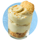 Close up of a glass with banana pudding parfait inside of it with sliced bananas on top, on a blue background.