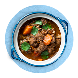 Overhead of a bowl of beef stew, on a blue background.