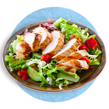  Close up of a wooden bowl with salad greens and a sliced chicken breast on top, on a blue background.