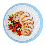 Overhead of a sliced chicken breast and a tomato salad on a white plate, on a blue background.