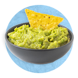 Close up of small blue bowl of guacamole with one tortilla chip dipped in it as decoration, on a blue background.