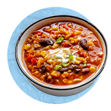Overhead of a chili bean soup in a white bowl, on a blue background.