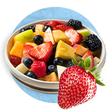 Close up of a fruit salad in a white bowl and a whole strawberry in front of bowl, on a blue background.