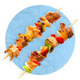 Close up of a pair of chicken and vegetable skewers, on a blue background.