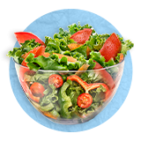 Close up of a glass bowl full of salad greens, tomatoes, and red peppers, on a blue background. 