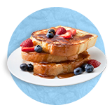 Close up of a stack of french toast with blueberries, Strawberries, and syrup, on a white plate with a blue background.