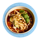 Overhead of a bowl of tortilla soup, on a blue background.