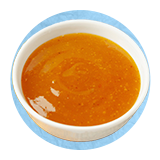 Close up of a white bowl full of salad dressing, on a blue background.