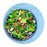 Overhead of a blue bowl full of salad greens, on a blue background.