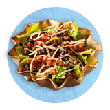 Close up of a taco salad in a tortilla bowl, on a blue background.