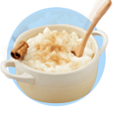 A dish of arroz con leche with cinnamon stick garnish and wooden spook on a blue background