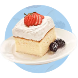 A slice of tres leches cake topped with sliced strawberries on a plate with blackberries in front of a blue background.