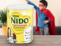 Nido Fortificada packaging on a table with a child in a super hero costume and plant in the background.
