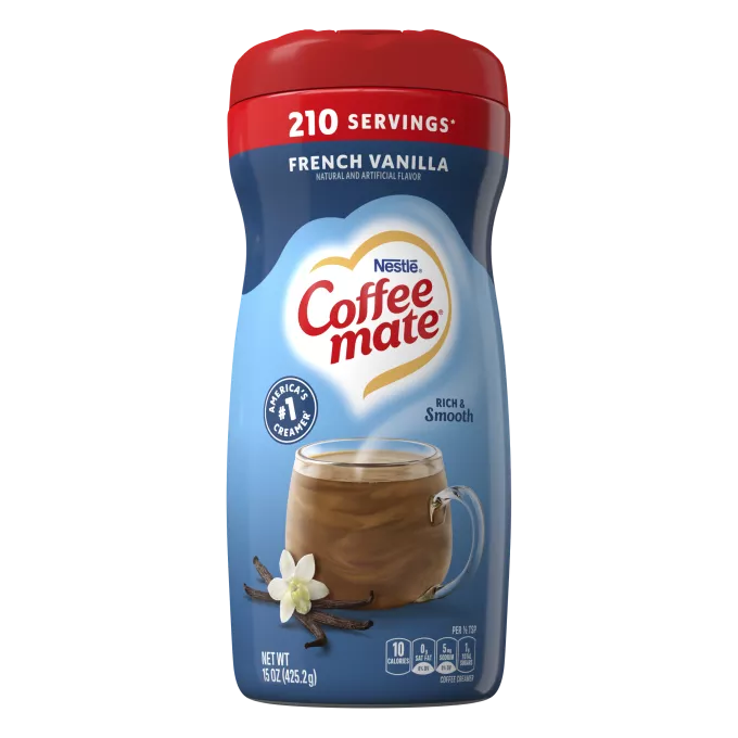 Una lata azul de creamer en polvo Coffee mate French Vanilla con una gorra roja encima de una taza de café y vainas de vainilla.