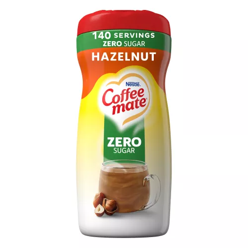 A canister of Hazelnut Powder with a green “sugar free” label above a coffee mug, whole hazelnuts and the product logo.
