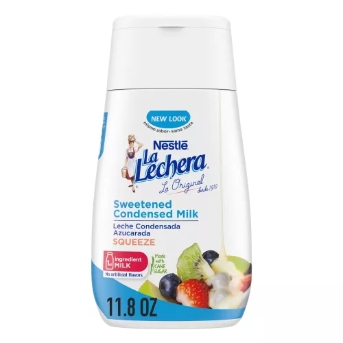 A squeeze bottle with a blue cap with the La Lechera logo beside a pile of fruit drizzled with sweetened condensed milk.