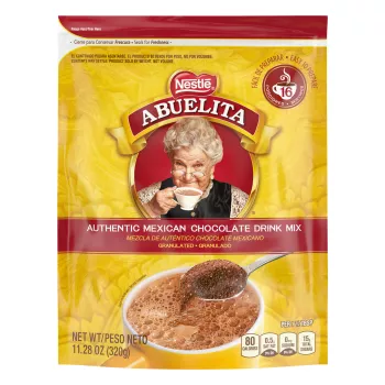 A yellow pouch with red labels and a spoon stirring hot chocolate mix into a yellow mug below the Abuelita logo.