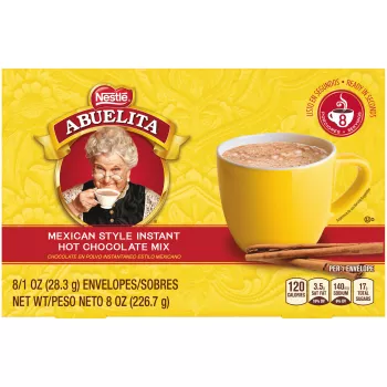 A yellow box with a red label below a yellow mug of Mexican hot chocolate behind cinnamon sticks.