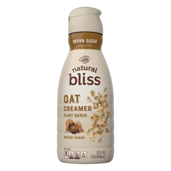 A brown bottle of natural bliss Oat Brown Sugar Creamer with a brown label above a measuring cup of brown sugar.