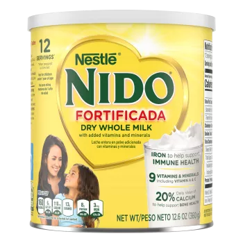 A canister of Nido Fortificada with a yellow label, white lid and gold heart above a glass of milk pouring.