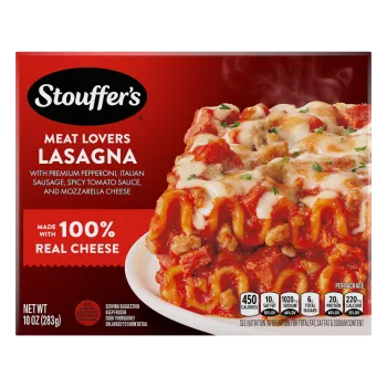 A plate of Meat Lovers Lasagna on a table below the product name, STOUFFER'S logo and "4 Delicious Meats" label.