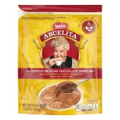 A yellow pouch with red labels and a spoon stirring hot chocolate mix into a yellow mug below the Abuelita logo.