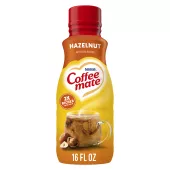 A bottle of Hazelnut Creamer with a red label  above a coffee mug, whole hazelnuts and the product logo.