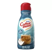 A blue bottle of Coffee mate Coconut Crème Creamer with a red cap and blue label above a coffee mug and coconut.