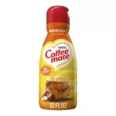 A bottle of Hazelnut Creamer with a red label above a coffee mug, whole hazelnuts and the product logo.