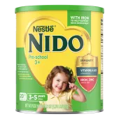 Vista frontal de la fotografía del envase cilíndrico para Nido 3+ con una etiqueta verde y amarilla brillante, una tapa verde y un corazón dorado sobre una foto de una niña sonriendo y señalando con una camisa amarilla pálida junto a un escudo que lee "inmunidad, vitaminas A, C y D, hierro y zinc"